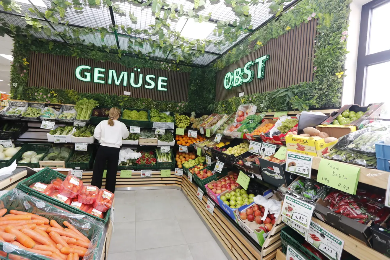 Helle Obst- und Gemüseabteilung von Hayat Market mit grüner Bepflanzung und beleuchteten Schildern Gemüse und Obst