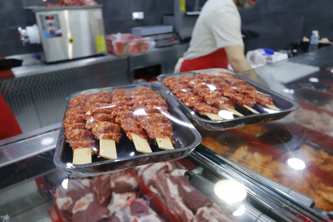 Frische Köfte-Spieße auf Tabletts über der Theke, im Hintergrund die Fleischwolf-Maschine der Hausmetzgerei
